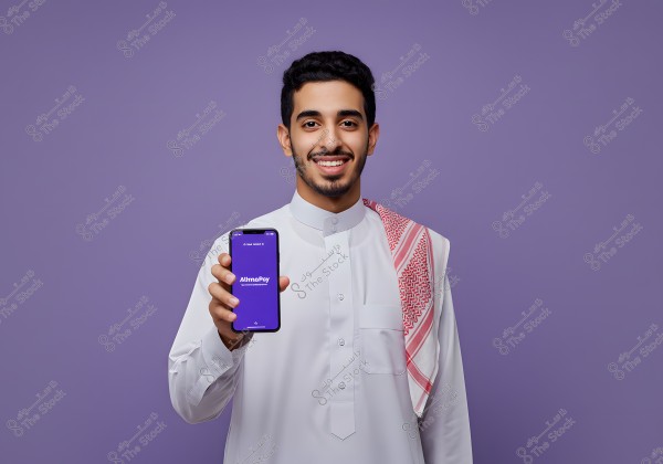 A portrait of a man wearing a white thobe and a red checkered ghutra, set against a purple background, holding a mobile phone displaying the \"AltimaPay\" logo. He appears happy and confident as he showcases the app on the phone.