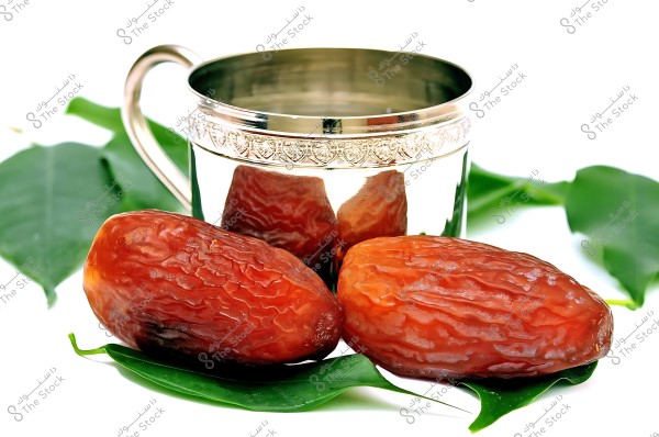 Large dates placed on green leaves with an ornate silver cup in the background.