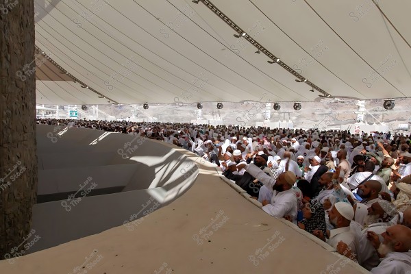 صورة لحجاج يرتدون ملابس الإحرام وهم يقومون برمي الجمرات أثناء مناسك الحج في منطقة مغطاة.