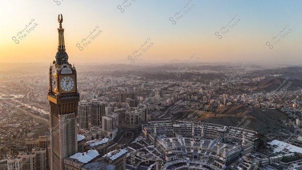Aerial view of the city of Mecca at sunset, featuring the Clock Tower prominently in the foreground, alongside the Grand Mosque filled with worshippers. The city stretches amidst the mountains, bathed in the warm colors of the setting sun.