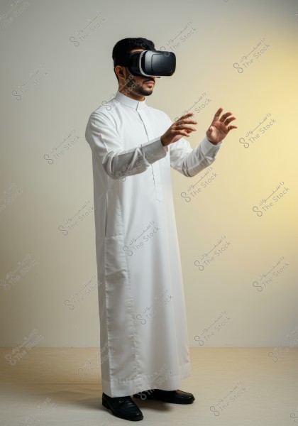 A man wearing a traditional white thobe and black virtual reality goggles, standing in an indoor environment with warm lighting. The thobe suggests that the image might be from Gulf countries like Saudi Arabia. The man is using the virtual reality goggles and interacting with his environment.