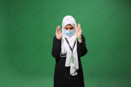 Portrait of a woman with white skin on a green background, wearing a mask and performing the duty of prayer