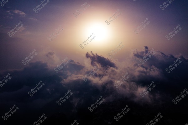 The image shows a natural scene of thick clouds covering the sky, with bright sunlight peeking through the horizon, providing soft lighting and warm colors. The background transitions from dark to light purple, indicating sunset or sunrise.