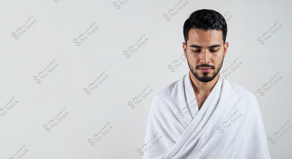 A portrait of a man against a white background, wearing a white wrap. The man has a beard and dark hair. The focus is on the upper part of his body, indicating it is a portrait. The style of clothing suggests he might be from Saudi Arabia or the Gulf region.