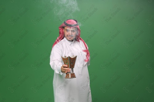 رجل سعودي يرتدي الزي التقليدي على خلفية خضراء ، التطيب بالبخور والعود ، استخدام خشب العود في المناسبات والأعياد.