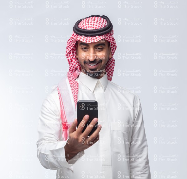 رجل سعودي يرتدي الزي السعودي الرسمي
 ويستخدم الجوال على خلفية بيضاء