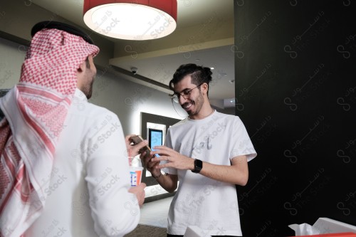 شاب سعودي يرتدي الزي السعودي التقليدي يعرض هاتفه المحمول للموظف ليتأكد من حجزه بينما يحمل بيده أحد المشروبات الغازية