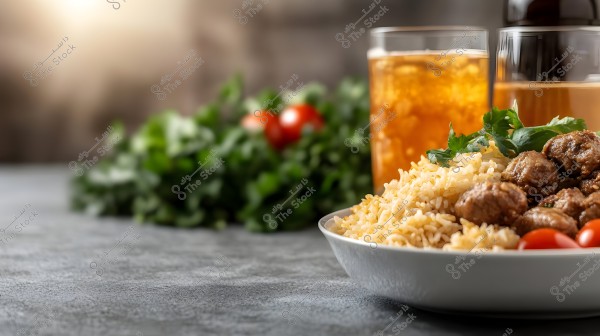 A plate of rice with meatballs garnished with parsley and small tomatoes sits on a table. In the background, there are two glasses with a cold drink and green ingredients with tomatoes as a garnish. The image focuses on the meal with a slight depth of field in the background.