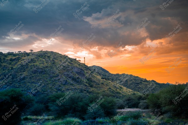 A natural view of a mountain covered with green vegetation during sunset, with a striking contrast between the colorful sky and dark clouds.