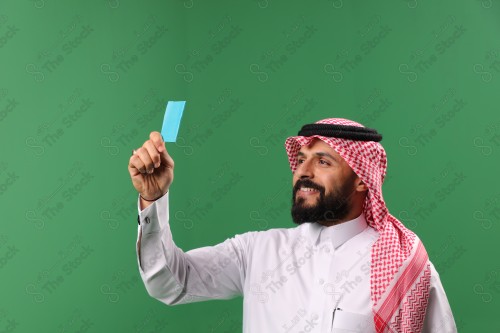 بورتريه رجل سعودي على خلفية خضراء مبتسم يحمل بطاقة الصرافة مستعد للتسوق