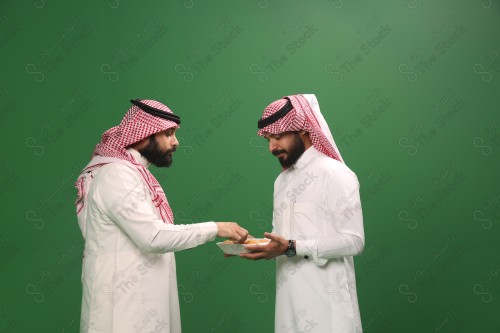 رجل سعودي يرتدي الزي السعودي التقليدي يقدم لضيفه طبق المعمول في أحد المناسبات