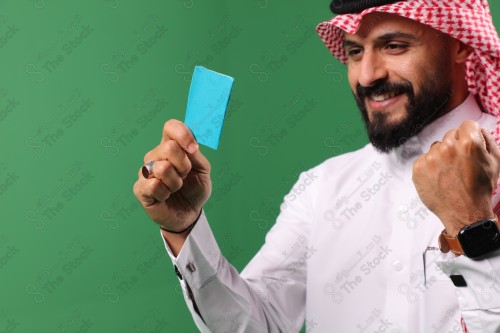 بورتريه رجل سعودي على خلفية خضراء متحمس يحمل بطاقة الصرافة مستعد للتسوق