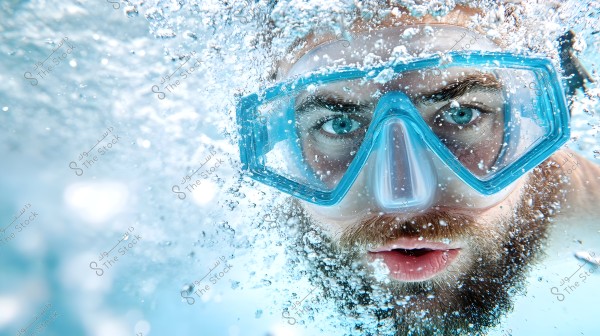 An image of a man underwater wearing blue diving goggles. The water is filled with bubbles, adding a dynamic feel to the photo. The man\'s face is shown up close, with his eyes clearly visible through the goggles.