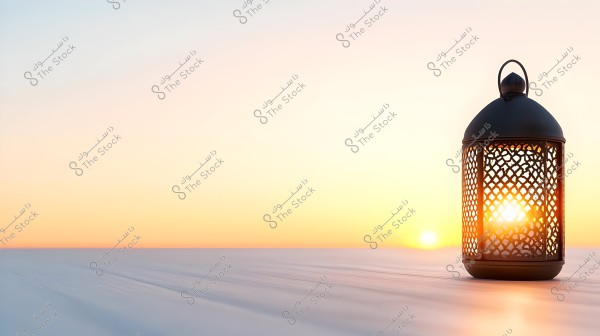 A decorative metal lantern with traditional designs is placed on a wooden surface, illuminated by the setting sun in the background, giving it a warm glow. The sky in shades of orange and yellow provides a calm and serene backdrop.