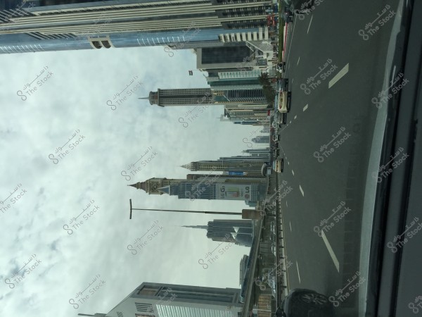 صورة لشارع مزدحم في مدينة حديثة تحتوي على ناطحات سحاب متعددة. يمكن رؤية السيارات تسير على الطريق السريع الواسع. تبرز مباني ناطحات السحاب بتصاميمها الزجاجية والحديثة, وتزين السحب السماء فوقها.