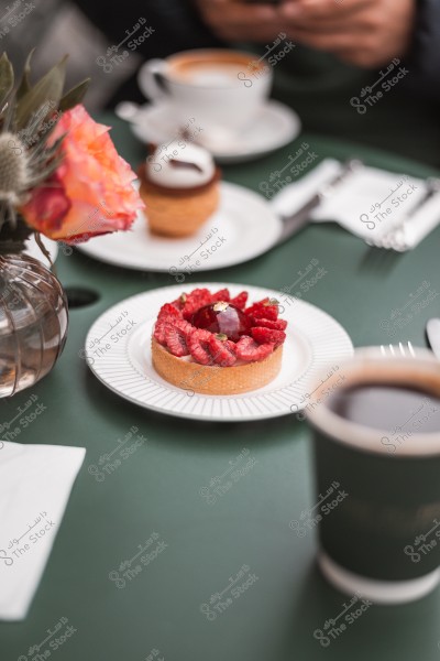 A raspberry tart served on a table with a cup of coffee and flowers on a green table.