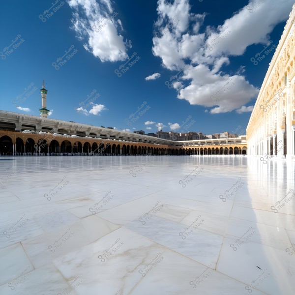 The image shows the courtyard of the Masjid al-Haram in Mecca, Saudi Arabia. The white tiles of the courtyard reflect sunlight under a clear blue sky with scattered white clouds. Golden minarets and columns frame the courtyard in distinctive Islamic architecture.