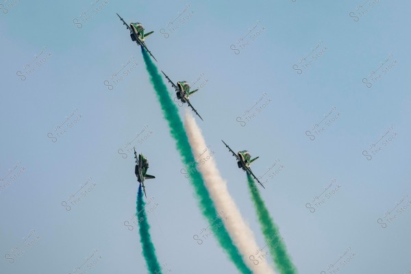 Four aircraft performing an air show, releasing smoke trails in white and green as they ascend in a formation angled upward against a clear blue sky.