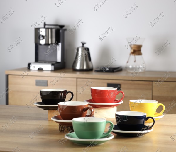 Colorful coffee cups on a wooden table with a coffee maker and kettle in the background.