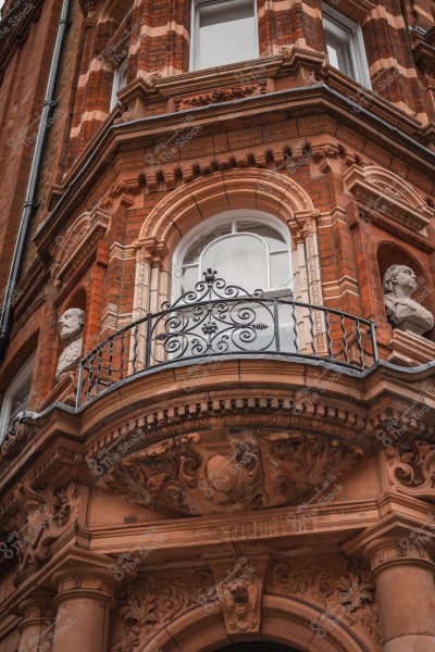 Red brick building facade with a decorative balcony and sculpted statues.