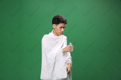 Portrait of a pilgrim with white skin on a green background wearing Ihram drinking water in several directions