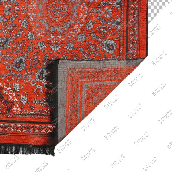 Image of a fabric with ornate patterns in orange, blue, and black colors. The design features traditional motifs, including floral shapes and geometric patterns, with a section turned over to reveal the differently colored reverse side.