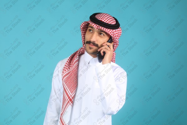 بورتريه رجل يرتدي الزي السعودي على خلفية تركواز، يتحدث بهاتفه وتبدوا على ملامحة السعادة، الاتصالات والتقنية