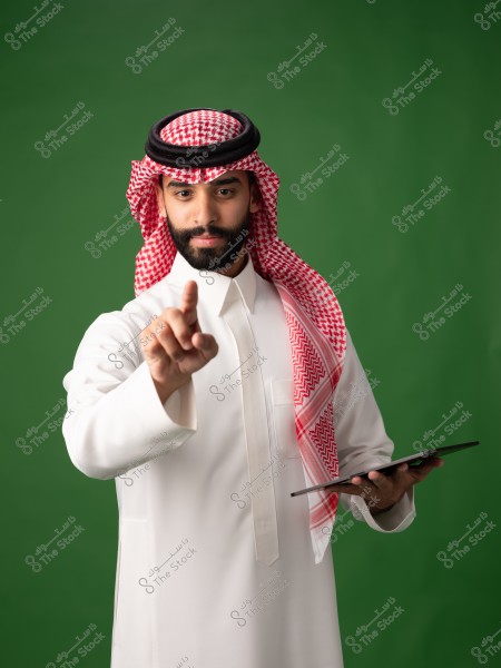 صورة لرجل يرتدي الثوب والشماغ التقليدي الخليجي باللونين الأبيض والأحمر. يقف الرجل أمام خلفية خضراء, ممسكًا بجهاز لوحي في يده اليسرى, بينما يشير بيده اليمنى نحو الأمام. الرجل يظهر وهو يرتدي العقال الأسود.