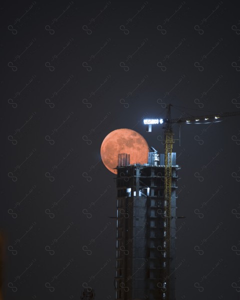 A shot of a building under construction with the big moon visible behind it at night, buildings and landmarks, sky.