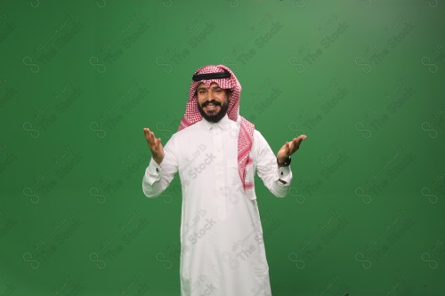 رجل سعودي يقف على خلفية خضراء يرتدي الثوب و الشماغ، يقوم بعمل حركات بيديه، يفتح ذراعيه وهو مبتسم، احتفالات العيد