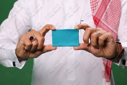 Saudi man on a green background holding a debit card, ready to shop