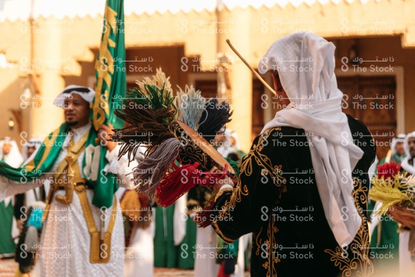 رجال سعوديون يرتدون الزي التقليدي يؤدون رقصة العرضة النجدية في قرية مبنية على الطراز التراثي