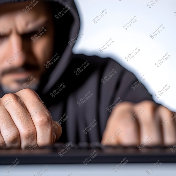 A photo of a man wearing a hoodie, focusing intently downwards while typing on a keyboard. The image is captured with a strong focus on the hands, highlighting the details as they engage with the keyboard.