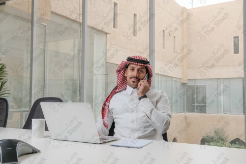 A Saudi man wearing the Saudi thobe sits in the meeting room and uses the mobile device