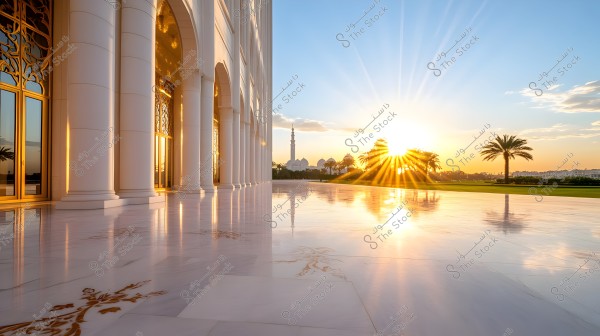 View of the sunset reflecting on the shiny marble surface of a large mosque courtyard. White columns and golden decorations adorn the scene, with the mosque\'s minaret and domes visible in the background. Palm trees on the sides add a natural touch.