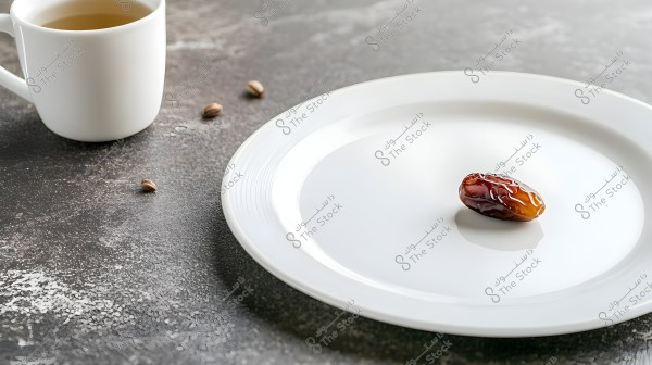 Image showing a single date placed in the center of a white plate on a gray surface. Adjacent to it is a white cup containing herbal tea, with some small date pits scattered on the surface.