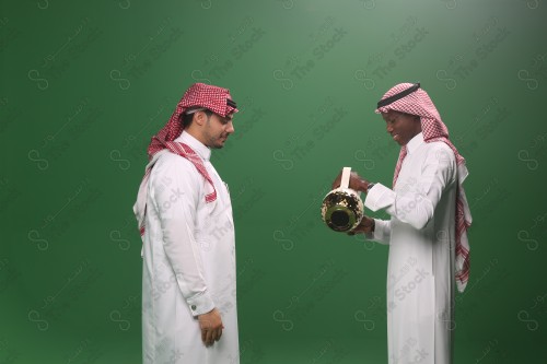 رجل سعودي يرتدي الثوب و الشماغ يقوم بسكب القهوة السعودية لرجل اخر