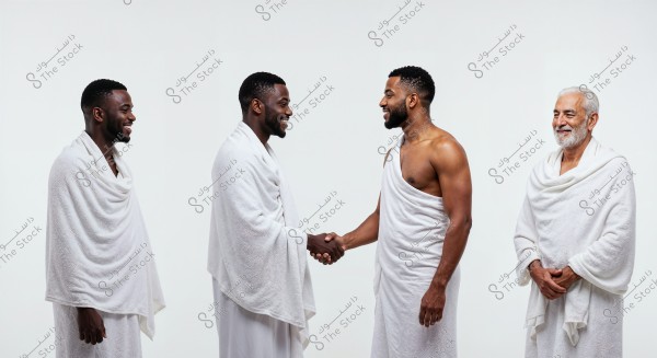 An image of four men standing side by side wearing white Ihram garments, which are used during Hajj and Umrah in Islam. The two men in the middle are shaking hands in a friendly manner, while the men on the ends are smiling. The background is white, highlighting their traditional white attire.
