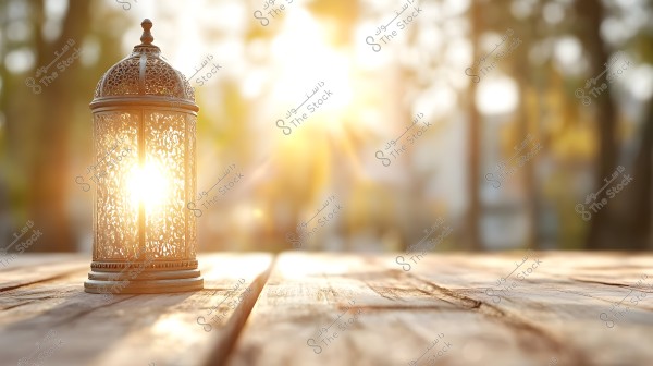 A traditional metal lantern with intricate decorative details placed on a wooden surface outdoors. The lantern is illuminated by bright sunlight shining through it, creating a warm and radiant atmosphere. The background features blurred lights and greenery, reflecting a serene natural setting.