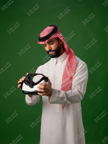 رجل عربي يرتدي الثوب التقليدي والغترة, يحمل نظارة واقع افتراضي بخلفية خضراء.