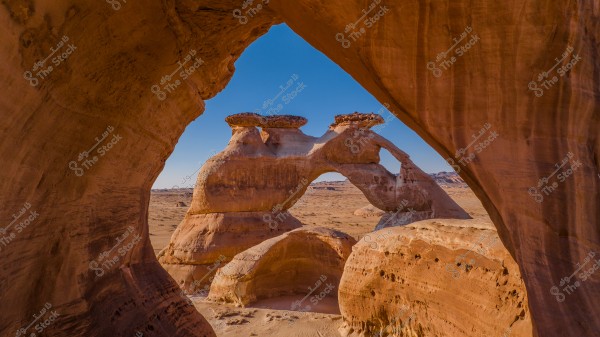 Stunning natural rock formations in the desert with two connected stone arches under a clear blue sky. The landscape extends with sand across the horizon and some small distant hills.