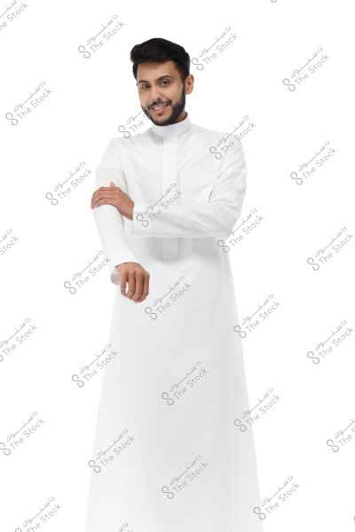 A portrait of a man wearing a traditional long white thobe, standing with a slight smile. The man appears to be folding the sleeves of his thobe, and the background is completely white. The thobe resembles traditional attire from the Gulf region, such as Saudi Arabia.