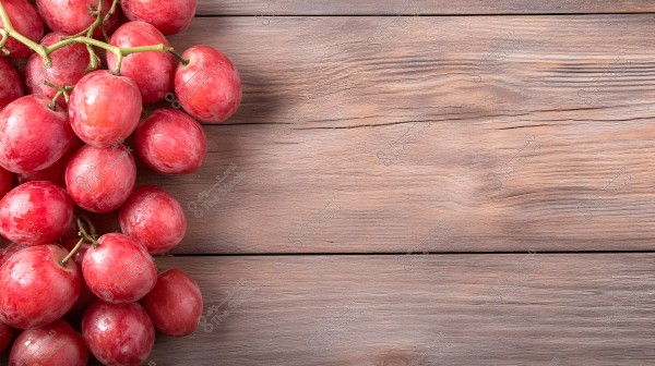 A bunch of red grapes on a brown wooden surface background. The left side of the image shows the grape cluster while the rest of the image displays the natural-colored wood.