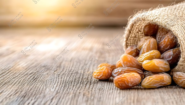 An image of fresh dates spilling out of a burlap sack onto a wooden surface. The dates appear golden-brown under warm lighting, with a blurred background that adds a warm glow.