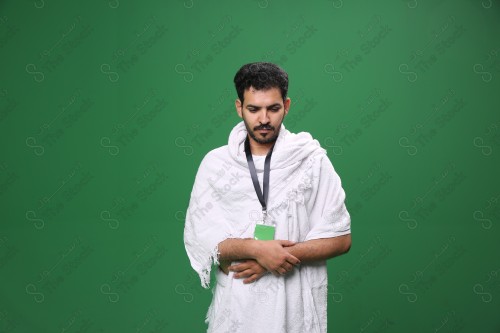 Portrait of a Saudi pilgrim on a green background wearing the Ihram to perform the Hajj rituals during prayer in several directions