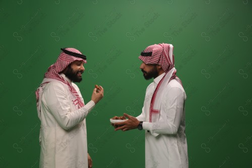 رجل سعودي يرتدي الزي السعودي التقليدي يقدم طبق من التمر لضيفه في أحد المناسبات