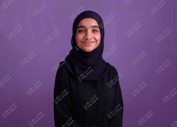 Portrait of a woman wearing a black hijab and a black abaya, standing against a purple background. The woman is smiling gently, facing the camera.