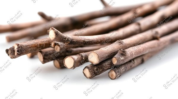 An image of a group of brown Miswak sticks placed on a white surface. The sticks are stacked irregularly, showing their cut ends, revealing the white interior of the sticks.