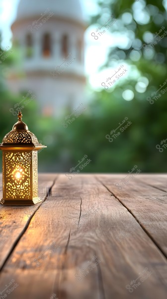 An ornate metal lantern glowing on a wooden table, with a blurred background of a mosque with a white dome and green trees.