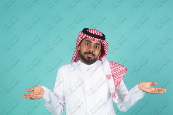 شاب سعودي على خلفية تركوازيه يعمل اشارات بيده ,تبدوا على ملامحه التعجب والاستغراب, ثوب و شماغ